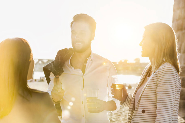 Business people celebrating success while drinking beer on the beach with lens flare in background - Foto, imagen