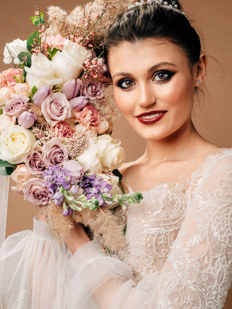 Wedding concept. Studio portrait of smiling brunette bride in wedding gown with bridal bouquet.  - Fotó, kép