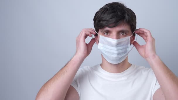Man puts a medical mask on her face on a gray background - Filmagem, Vídeo
