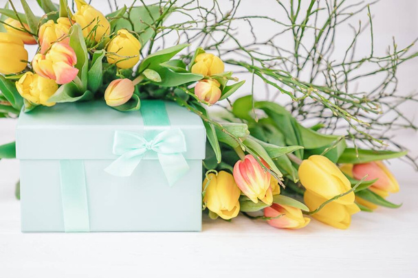 Delicate elegant gift box and a lot of spring yellow tulips on a white background - Fotó, kép