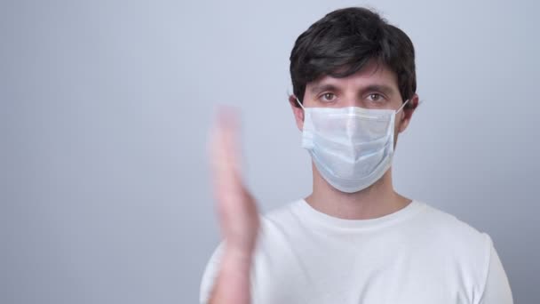 Man in a medical mask showing and presenting with open hand palm on a gray background. - Кадри, відео