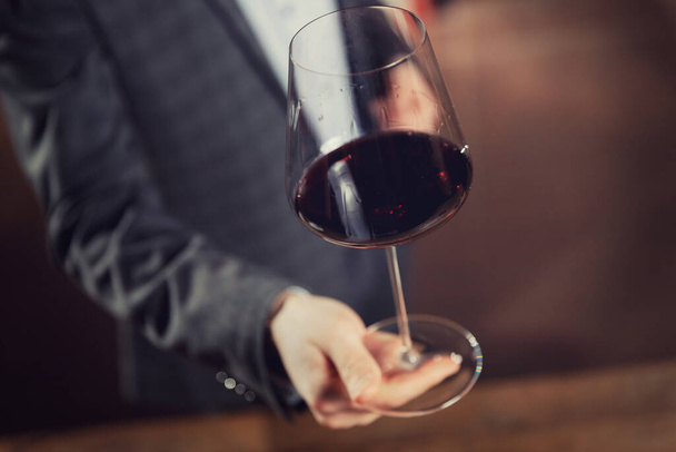 Waiter serves glass of red wine in restaurant, dark background - Photo, image