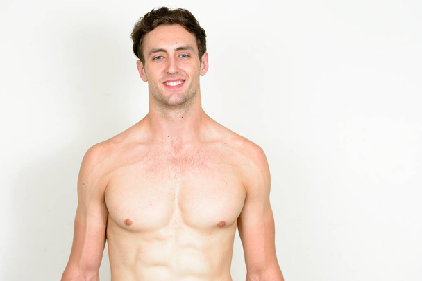 Studio shot of young handsome muscular man with wavy hair shirtless against white background - Zdjęcie, obraz