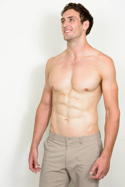 Estúdio tiro de jovem homem musculoso bonito com cabelo ondulado sem camisa contra fundo branco - Foto, Imagem