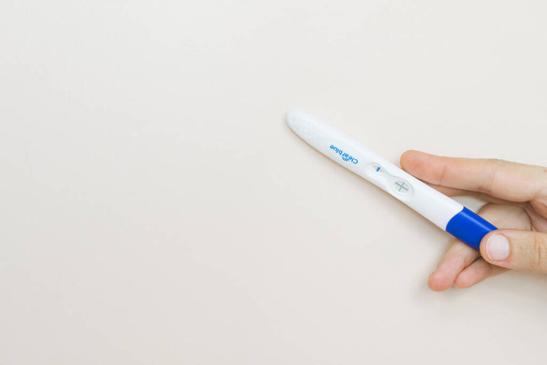 Vrouw hand met een positieve zwangerschapstest op roze achtergrond. - Foto, afbeelding