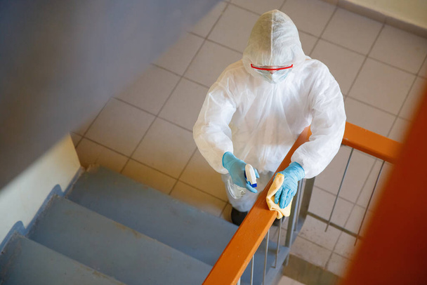 Концепция дезинфекции коронавируса. Люди в hazmats делает чистку перила лестницы многоквартирного дома
 - Фото, изображение