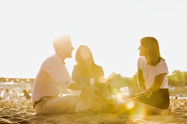 Business people celebrating success while drinking beer on the beach with lens flare in background - Fotoğraf, Görsel