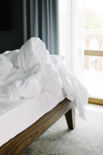 Large white bed standing in the room. Crumpled sheet and blanket. - Foto, Imagem