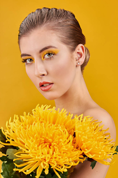 Blonde woman with light eyes naked with yellow flowers on yellow background - Photo, Image