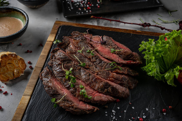Plátky grilované hovězí barbecue Striploin steak s omáčkou chimichurri na prkénku na tmavé dřevěné pozadí - Fotografie, Obrázek