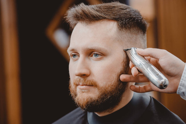 Hairdresser cuts hair young men in barbershop. Barber doing styling with electric shaver - Foto, Bild