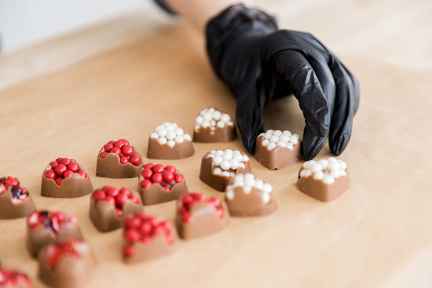 Banketbakker toont zelfgemaakte zoete chocolade snoepjes in de vorm van rode en witte hartvormige vulling - Foto, afbeelding