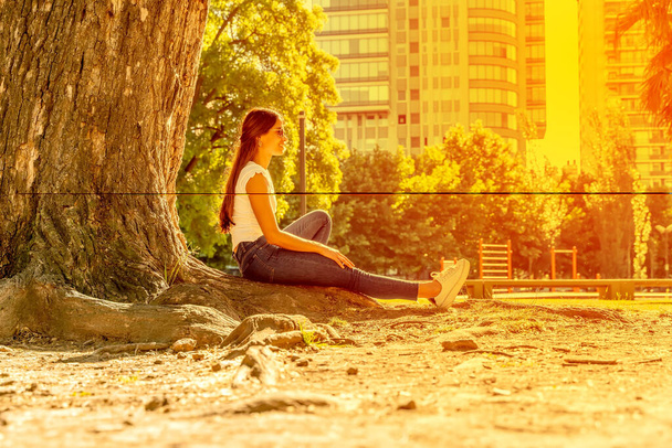 A young woman sitting next to a tree and enjoying the sunshine - Foto, Bild