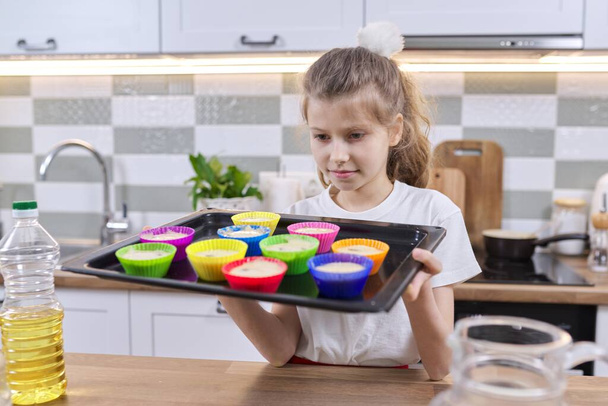 Child girl in apron in kitchen with tray of preparing raw silicone cupcakes. Home cooking, homemade food, cooking with children - Foto, Imagen