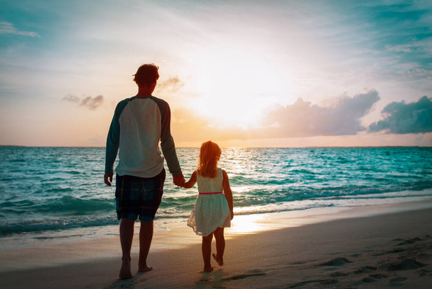 father and little daughter walking on beach at sunset - 写真・画像