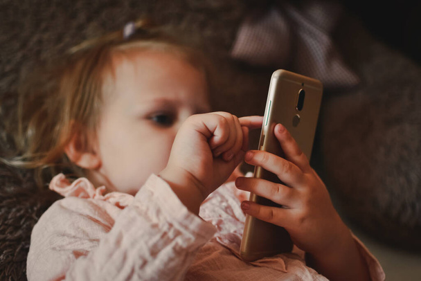 Beautiful little girl watching cartoons on a smartphone. Video communication. Online call to friends. The distance of friends. Teaching children online. A child plays on a smartphone. Leisure at home - Photo, Image