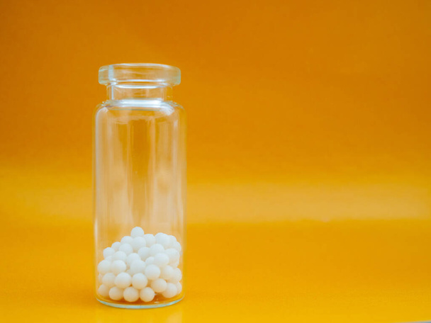 Homeopathische bolletjes en glazen fles op gele achtergrond. Homeopathische Geneeskunde - Foto, afbeelding