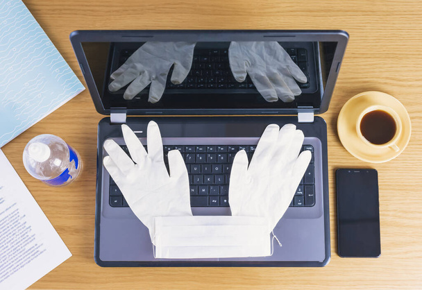 Górny widok obszaru roboczego podczas Covid19 Coronavirus rozprzestrzenia się z laptopem, maską do nosa, okularami, filiżanką i środkiem do dezynfekcji rąk. - Zdjęcie, obraz