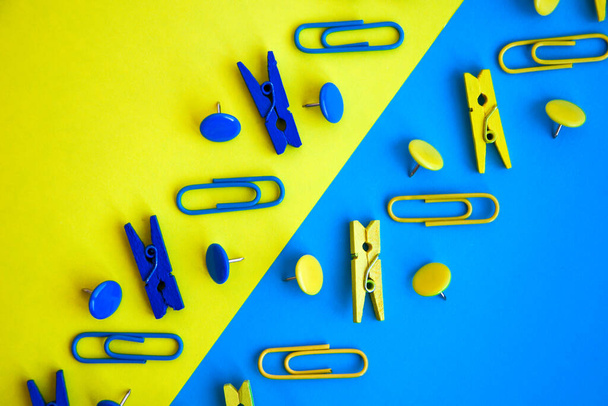 Irodai kellékek színes gombok és gemkapcsok, sárga és kék hátterű ruhák, másolótér, határ és keret formájában, vissza az iskolába - Fotó, kép