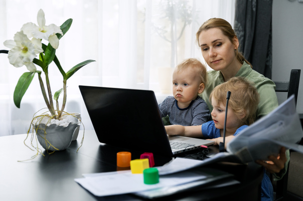 mother working from home. using laptop at desk with kids on her lap - Zdjęcie, obraz