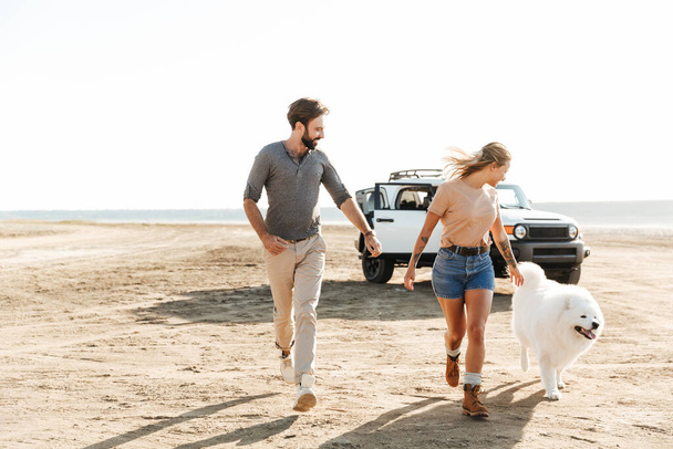 Attractive young couple playing with their dog at the sunny beach - Foto, Imagen
