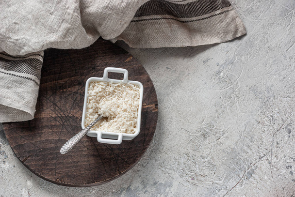 Coconut flakes in a square square bowl with handles on a wooden round board on a concrete tabletop background. Culinary cover, ingredient - Foto, immagini