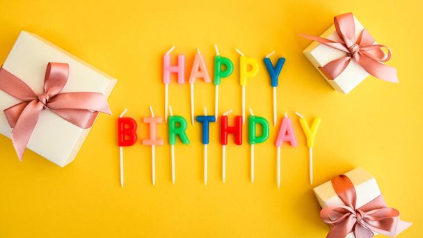Happy Birthday candles on yellow background. Bright color wallpaper Candles with text Happy Birthday present boxes - Photo, Image