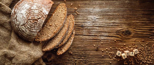 Tradycyjny zakwaszony chleb zakwaszony pokrojony w plasterki na rustykalnym drewnianym tle z przestrzenią do kopiowania, widok z góry. Pojęcie tradycyjnych metod wypieku chleba liściastego - Zdjęcie, obraz