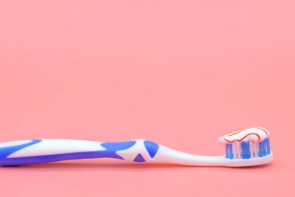ピンクの背景に歯磨き粉の赤い渦を持つ白い歯ブラシ。歯科と医療の概念. - 写真・画像