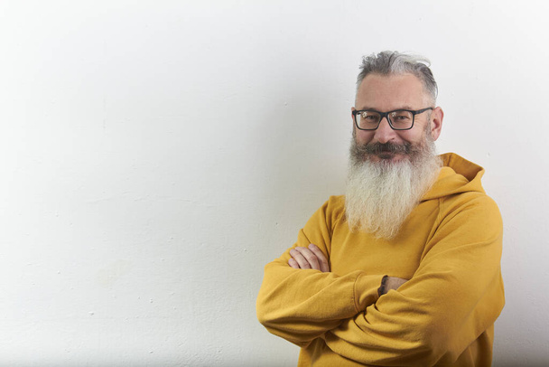 Portrait of mature gray-haired bearded man in yellow hoodie on white backdrop, selective focus - Foto, Imagen