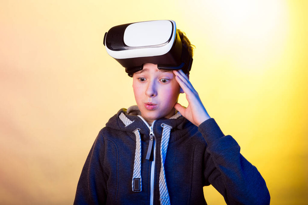 Emotionen und Freude eines jungen Mannes bei der Nutzung virtueller Realität. Foto eines jungen Mannes in einer dunklen Sportjacke auf einem Hintergrund von vorherrschenden gelben und hellvioletten Farbtönen - Foto, Bild