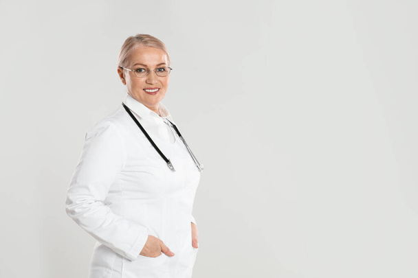 Portrait of mature doctor with stethoscope on light grey background. Space for text - Fotoğraf, Görsel