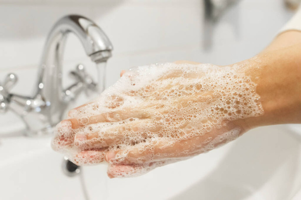 Frotar las palmas, lavarse las manos con jabón antibacteriano y en la técnica adecuada sobre el fondo de agua corriente en el baño blanco. Prevención coronavirus. Limpieza y desinfección de manos
 - Foto, Imagen