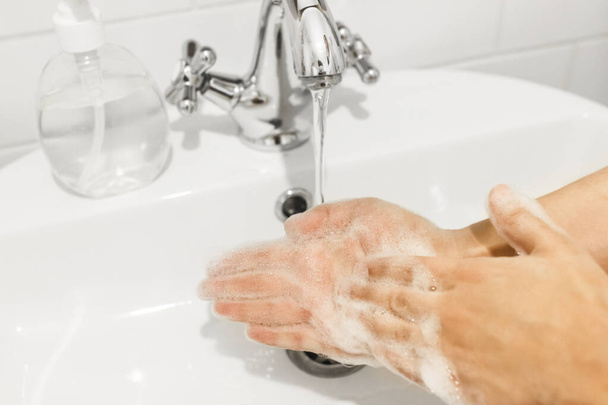 Lavarse las manos. Frotar las palmas, lavarse las manos con jabón antibacteriano y en la técnica adecuada sobre el fondo de agua corriente en el baño blanco. Prevención coronavirus. Limpieza y desinfección de manos
 - Foto, Imagen