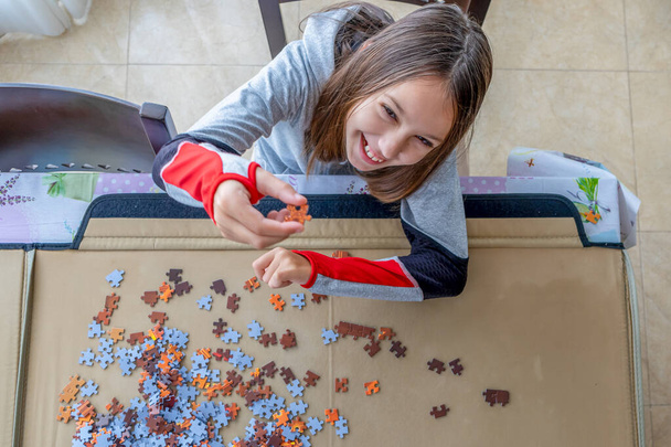 Mooi klein meisje in sporttrainingspak die puzzelt in haar woonkamer. Ontvangstconcept - Foto, afbeelding