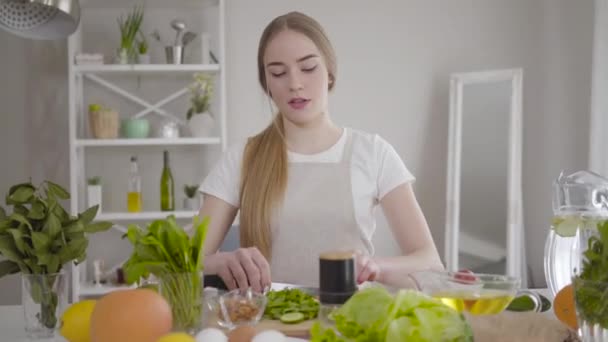 Портрет молодой уверенной белой женщины, вырезающей ингредиенты для органического салата в помещении. Девочка готовила еду дома. Здоровый образ жизни, вегетарианство, здоровье
. - Кадры, видео