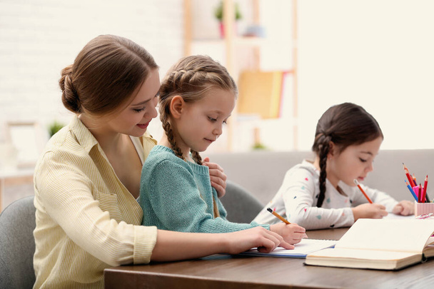 Mother helping her daughters with homework at table indoors - Photo, image