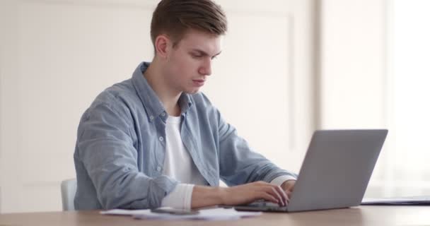 Young concentrated guy typing on laptop at home office - Video