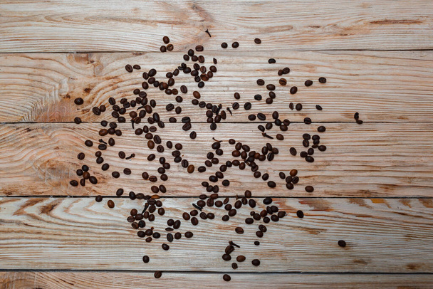 Verstreute Kaffeebohnen und Nelken auf einem hellen Holztisch. Draufsicht, Platz für Text. Selektiver Fokus - Foto, Bild