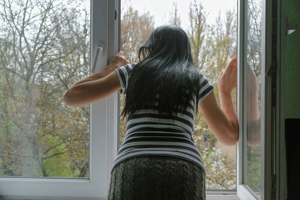 Donna di 60 anni con i capelli lunghi neri guarda fuori dalla finestra. Da solo a casa
. - Foto, immagini