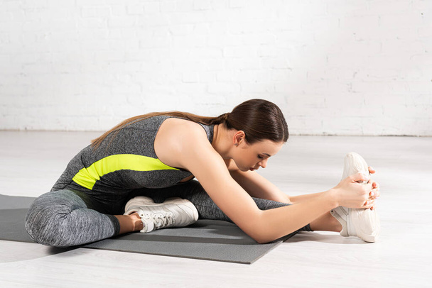 young and flexible sportswoman warming up on fitness mat  - Foto, imagen