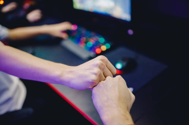 Professional gamer greeting and support team fists hands online game in neon color blur background. Soft focus, back view - Φωτογραφία, εικόνα