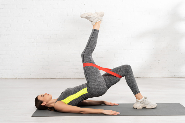 вид сбоку спортивной женщины, упражняющейся с лентой сопротивления на фитнес-коврике
 - Фото, изображение
