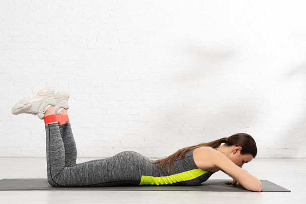 sportive woman lying on fitness mat and working out with resistance band - Foto, imagen