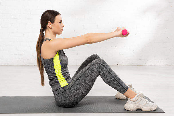 profile of young sportswoman exercising with pink dumbbells on fitness mat - Photo, Image