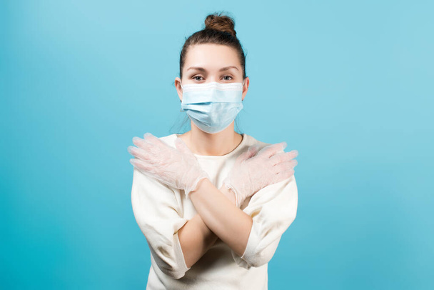 Young woman paramedic in medical mask and gloves crosses her arms over her chest. Isolated on a blue background - Fotoğraf, Görsel