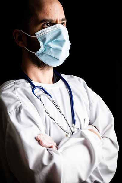 Portrait of a male doctor wearing a mask and a stethoscope against a seemless black background - Fotoğraf, Görsel