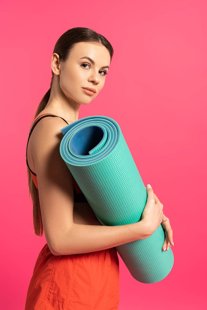 attractive sportswoman holding fitness mat isolated on pink  - Fotó, kép