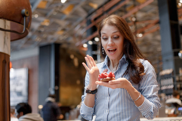 Beautiful girl in a blue shirt is surprised at a beautiful mouth-watering strawberry dessert. - 写真・画像