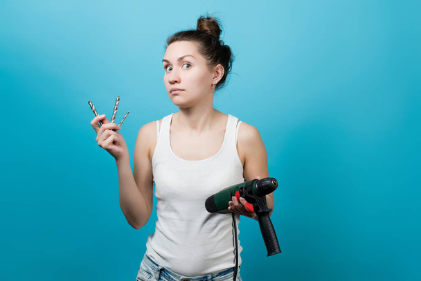 The girl holds a drill with drills and looks frightened, not understanding what everyone needs to do with this and how - Foto, imagen